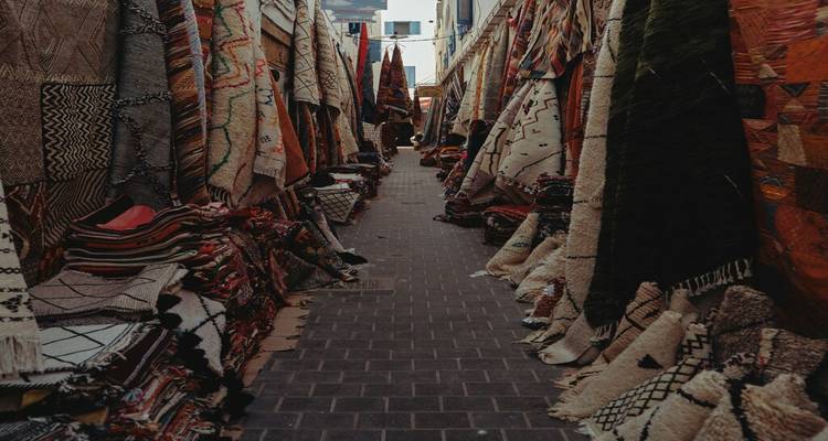 Une ruelle étroite du souk, remplie de tapis et de tapis tissés colorés empilés en hauteur, s'étend dans les ombres.