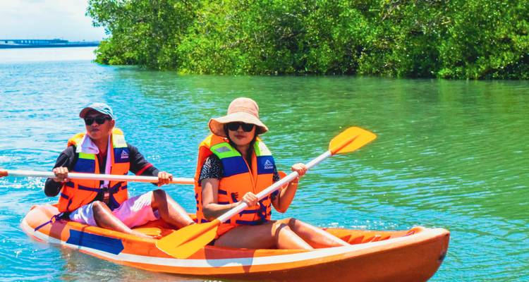 Deux pagayeurs dirigeant un kayak orange sur un lagon cristallin avec des palétuviers en arrière-plan.