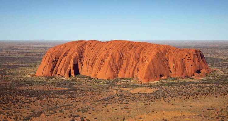 Vue aérienne du monolithe massif de grès rouge Uluru entouré de plaines arides.