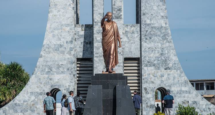 Statue en bronze de Kwame Nkrumah se dressant devant un mausolée en marbre entouré de visiteurs.