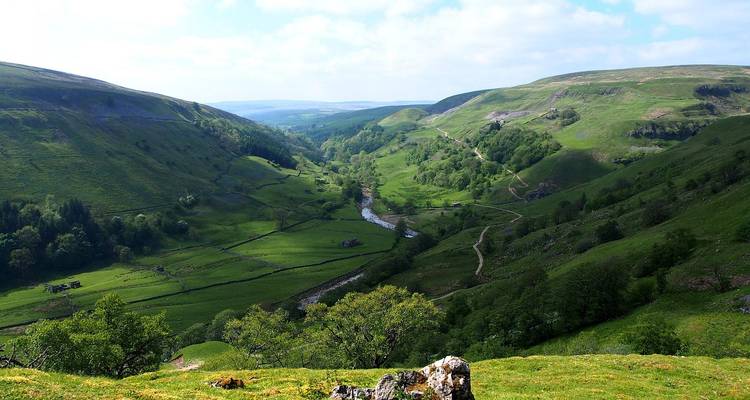 La vallée verte et spacieuse avec sa rivière sinueuse et ses prairies en damier s'étend jusqu'aux collines lointaines des Yorkshire Dales.