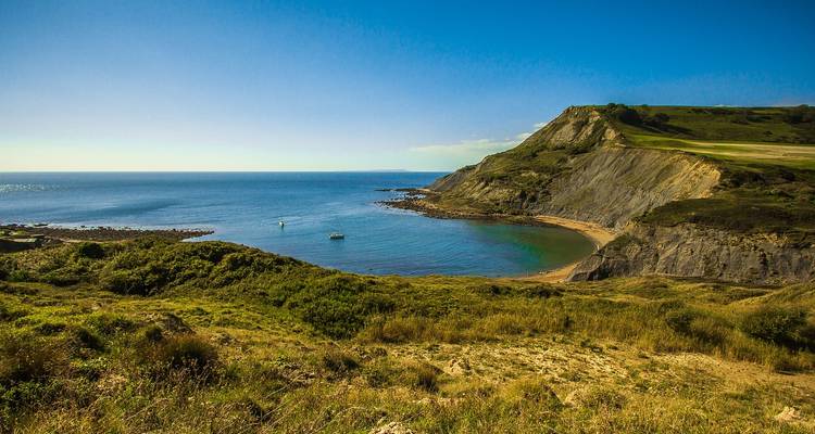 Turquoise bay fringed by rugged green headlands and high cliffs meets the endless blue Atlantic coast of Cornwall.