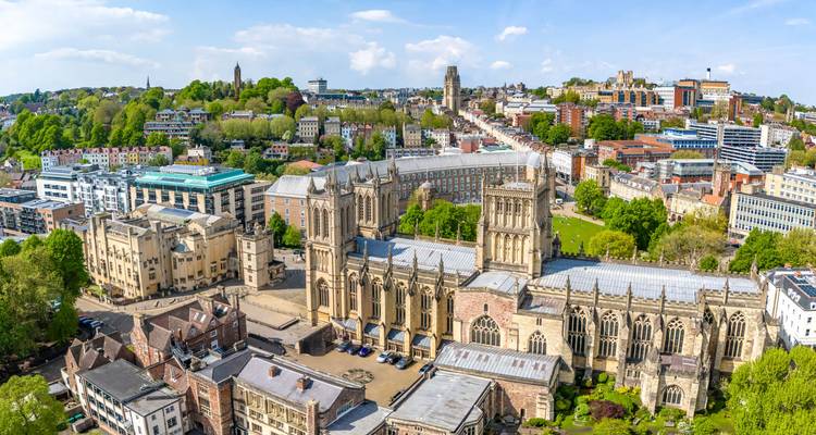 Panoramic aerial of Bristol showing the gothic cathedral, leafy parks, and colourful cityscape on a bright spring day.