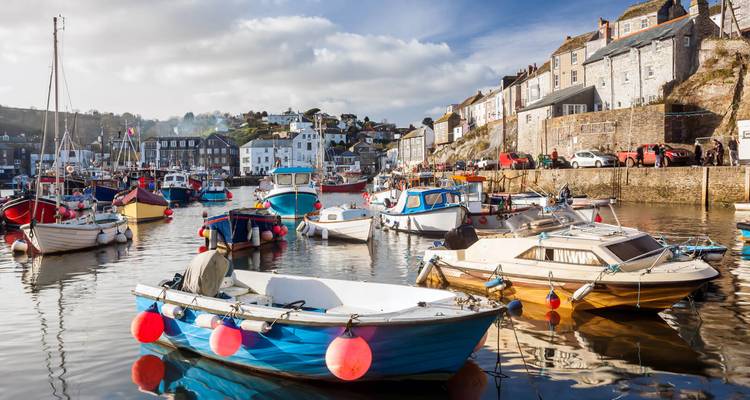 Charming harbour packed with colourful fishing boats reflecting in calm water, stone quays and cottages on a sunny day.