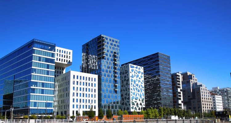 Modern glass and steel buildings of Oslo’s Barcode district against a vivid blue sky.
