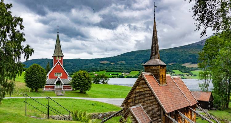 Two picturesque wooden churches by a lake with dramatic clouds and green countryside around.