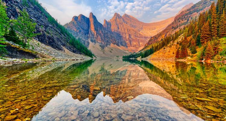 Crystal-clear alpine lake reflecting dramatic spires and golden morning light in the Canadian Rockies.
