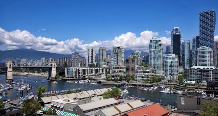 View over Granville Island Public Market toward Vancouver’s high-rise skyline under fluffy clouds.
