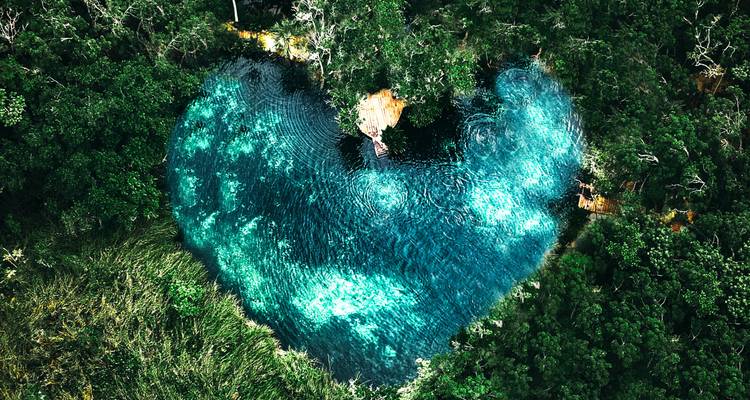 Drone view of a heart-shaped vivid turquoise lagoon surrounded by dense tropical jungle.