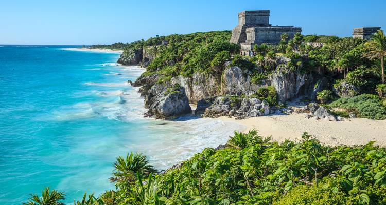 Turquoise Caribbean waters crashing against limestone cliffs topped with ancient Mayan ruins at Tulum.