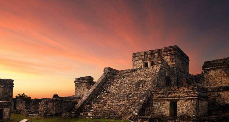 Les anciennes structures de pyramides en pierre de Tulum se détachant en silhouette contre un ciel de coucher de soleil d'un orange éclatant.