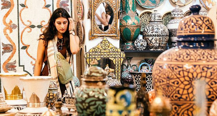 A young woman browses intricate Moroccan ceramics and pottery in a vibrant market stall.