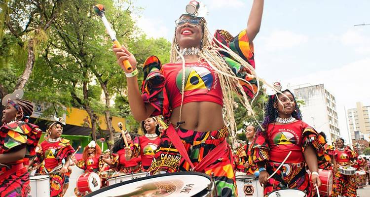 Energetic drummers in colorful carnival costumes perform joyfully in a lively street parade.