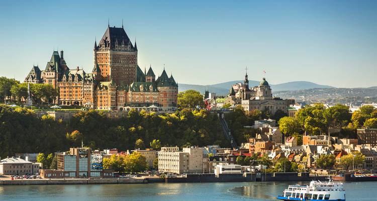 Vue panoramique de la Ville de Québec avec le château Frontenac emblématique s'élevant au-dessus des bâtiments historiques le long du fleuve Saint-Laurent sous un ciel bleu dégagé.