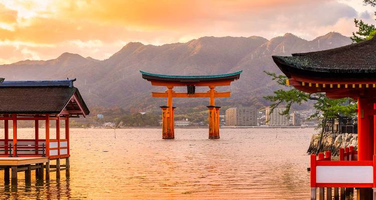 Iconic vermilion torii gate of Miyajima rises from shimmering water under a warm sunset sky.