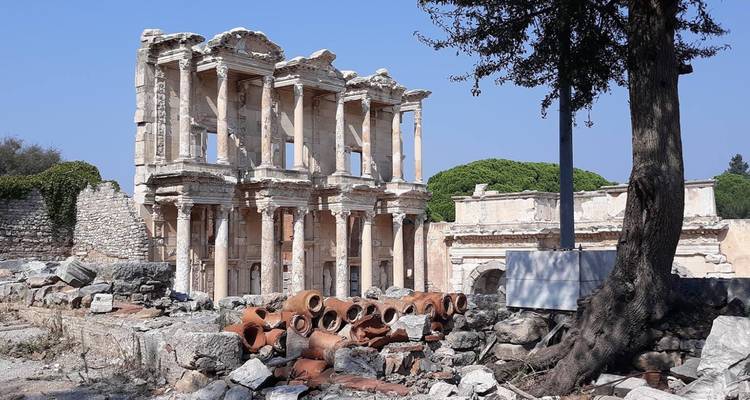 Façade en pierre bien conservée d'une ancienne bibliothèque romaine entourée de ruines éparses et d'amphores.