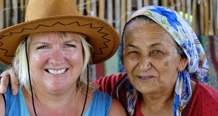 Portrait en gros plan de deux femmes souriantes, l'une portant un chapeau de cowboy, l'autre un foulard floral sur la tête.