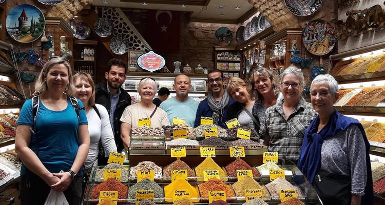 Groupe de voyageurs souriants à l'intérieur d'une boutique d'épices colorée remplie de bacs étiqu etés d'herbes et d'épices.