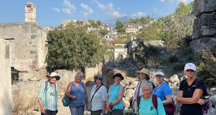 Groupe de touristes posant parmi les ruines de pierre et la végétation envahissante sous un ciel bleu éclatant.