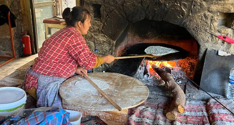 Femme préparant du pain plat dans un four traditionnel chauffé au bois à l'intérieur d'une cuisine rustique en pierre.