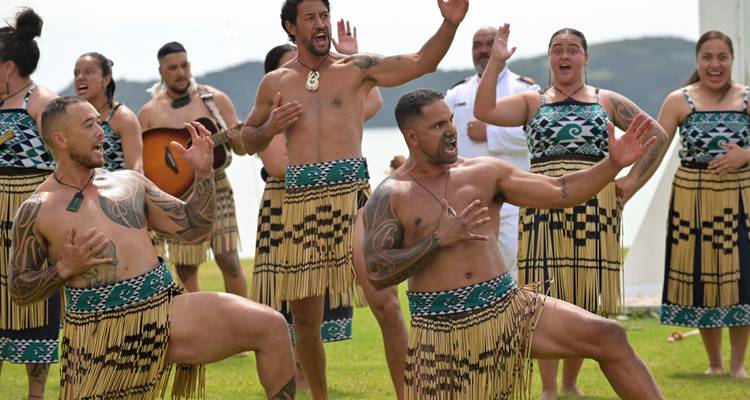 Maori performers in traditional dress energetically dancing the haka near the water