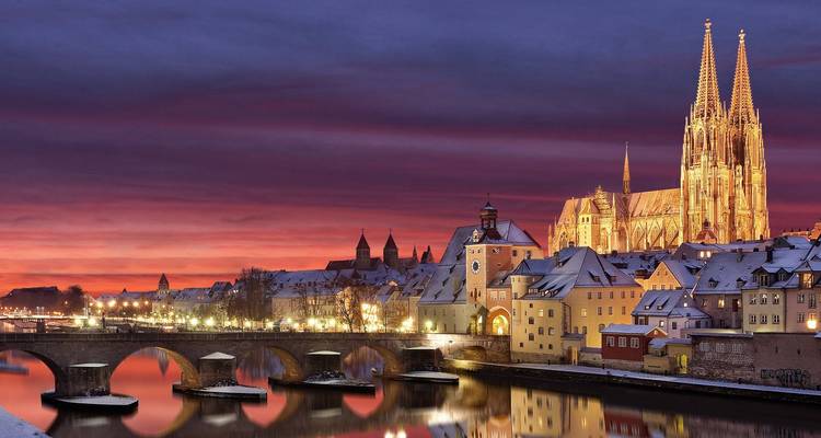 Snow-covered medieval skyline of Regensburg glows under a dramatic purple-red winter twilight.