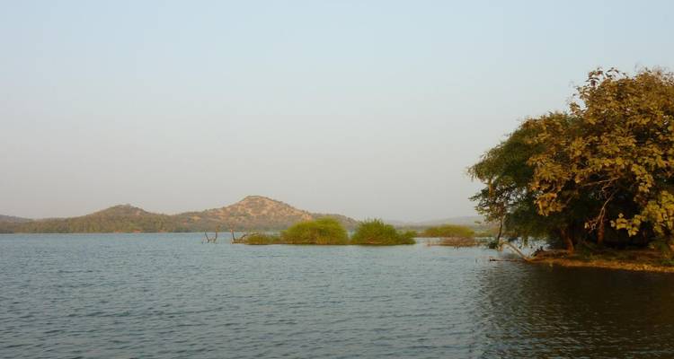 A tranquil inland lake with small islands and hazy hills under a pale sky.