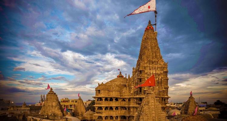 The ornate Dwarkadhish Temple crowned with flags set against a dramatic cloudy sky.