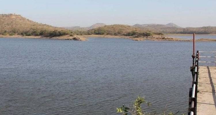 A sparsely vegetated reservoir with dry hills in the background viewed from a concrete pier.