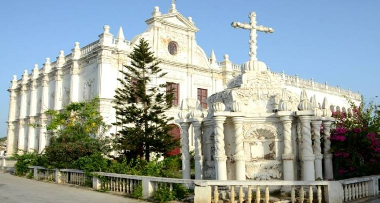 The white façade of St. Paul's Church in Diu with ornate cross and garden in foreground.