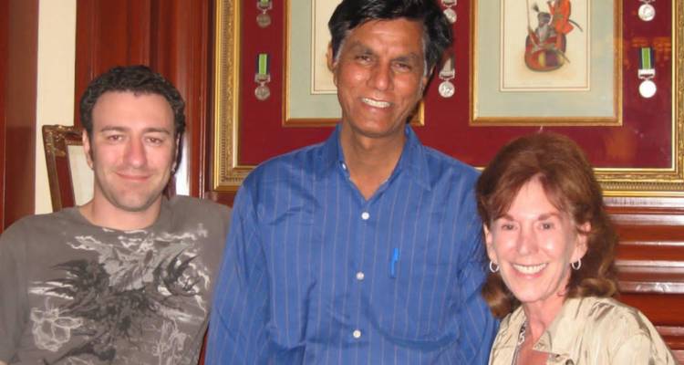Three adults smiling and posing inside a richly decorated interior with framed medals on a red wall