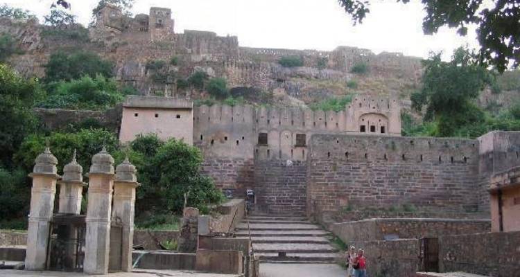 Stone steps lead up to the historic Ranthambore Fort walls amid greenery with two visitors exploring.