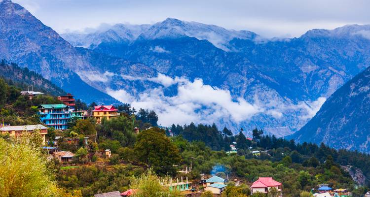 Village de montagne coloré perché sur des pentes luxuriantes avec des pics enneigés dramatiques de l'Himalaya en arrière-plan.