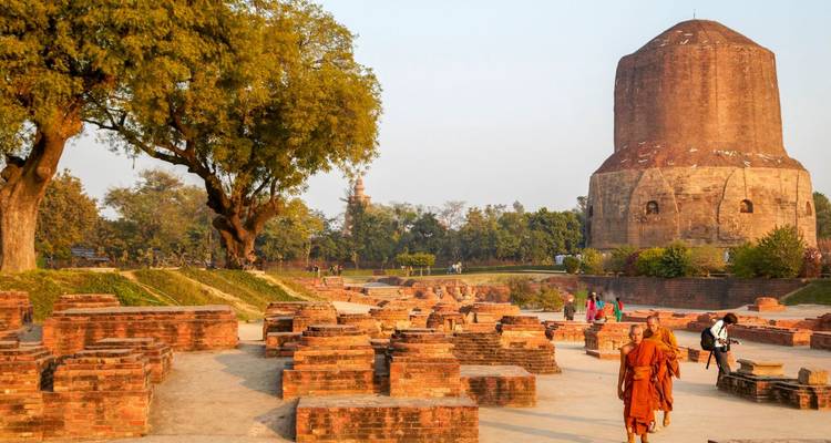 Des moines vêtus de robes safran marchent parmi les anciennes ruines de briques face au majestueux Dhamek Stupa au coucher du soleil.