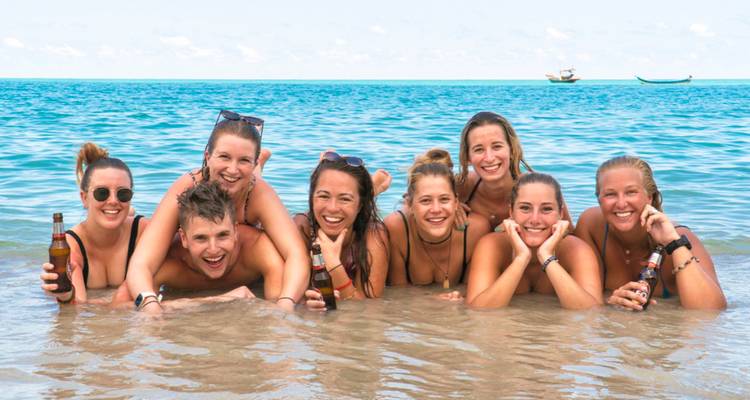 Group of friends lying in shallow tropical water laughing and holding bottles