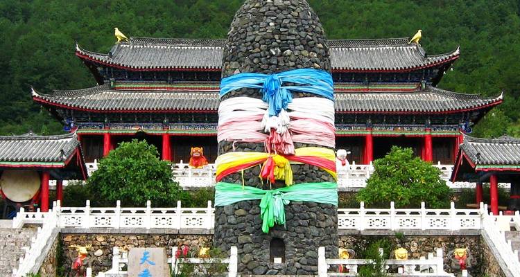 Monument en pierre enveloppé de draps de prière colorés se dressant devant une architecture orientale ornée.