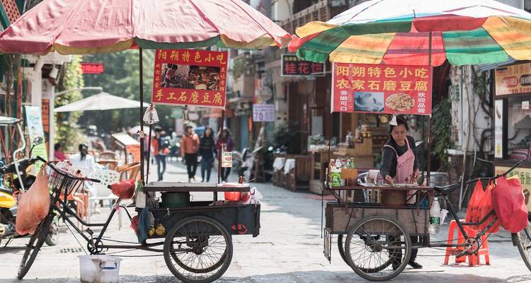 Un vendeur ambulant avec des parapluies colorés vend des en-cas à partir d'un chariot tricycle le long d'une ruelle pavée.