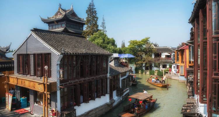 Ville canalaire pittoresque avec des maisons aux toits en tuiles et des bateaux glissant sur l'eau émeraude sous un ciel bleu dégagé.
