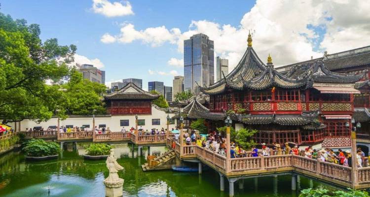 Complexe de pavillons chinois historiques à côté d'un étang rempli de visiteurs ; des gratte-ciel modernes se dressent en arrière-plan.