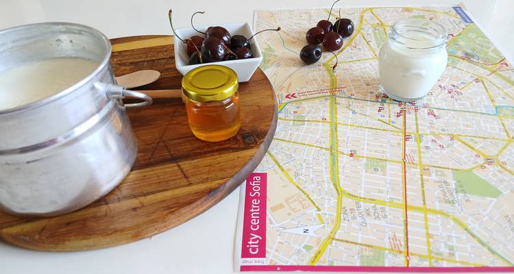 Nature morte composée de yaourt, de miel, de cerises et d'une carte du centre-ville de Sofia disposés sur un plan de travail blanc.