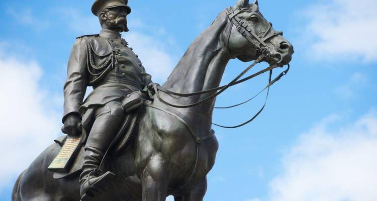 Statue équestre en bronze d'un chef en uniforme à cheval se détachant sur un ciel bleu éclatant.