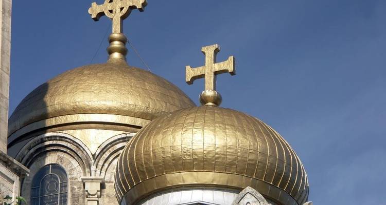 Deux dômes orthodoxes dorés et scintillants, surmontés de croix, s'élèvent contre un ciel bleu limpide.