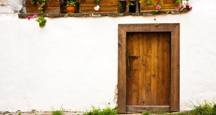 Porte en bois rustique enchâssée dans un mur blanchi à la chaux avec des pots de fleurs colorés suspendus au-dessus.