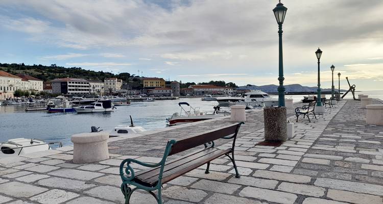 Promenade en pierre bordée de bancs et de lampadaires surplombant une marina à l'aube