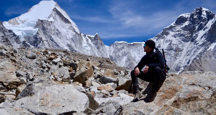 Einzelner Trekker ruht auf einem Felsen mit dramatischem Blick auf die Himalaya-Gipfel in der Nähe von Gorak Shep.