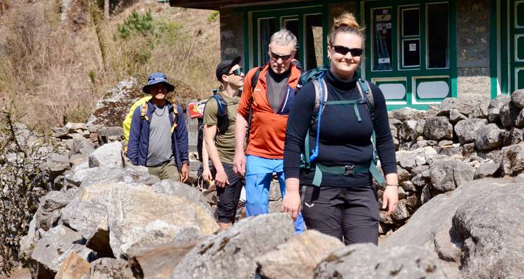 Lächelnde Trekker, die auf dem EBC-Weg durch Steinhäuser eines Dorfes gehen.