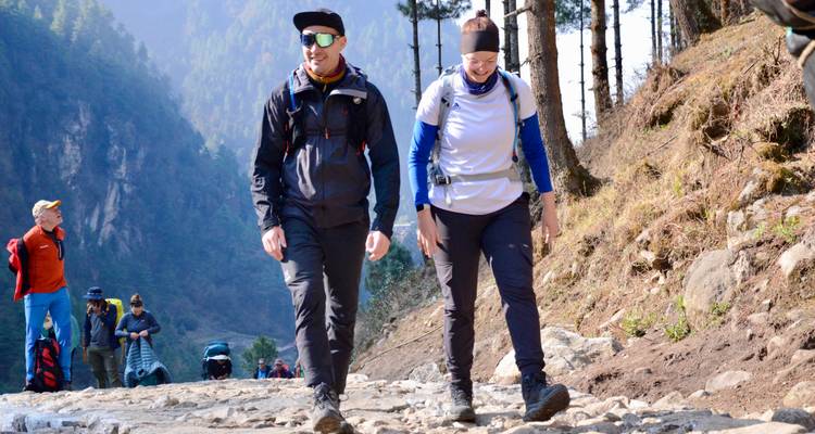 Trekkingpaar, das auf einem Steinweg durch ein bewaldetes Himalaya-Tal wandert.
