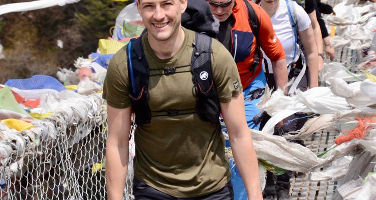 Lächelnder Wanderer überquert eine mit Gebetsfahnen bedeckte Hängebrücke in Nepal.