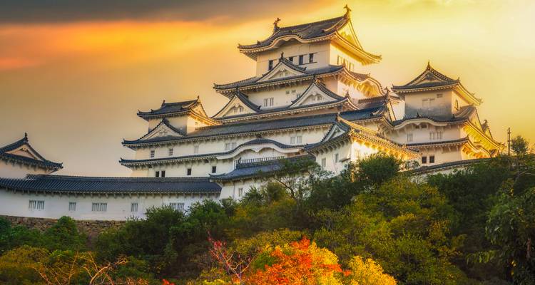 Himeji Castle glowing at sunset with autumn foliage in the foreground.