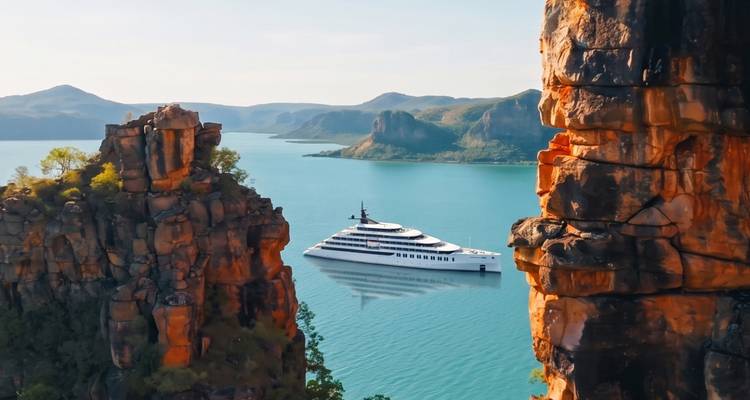 Luxury white yacht anchored in turquoise bay framed by towering orange cliffs.